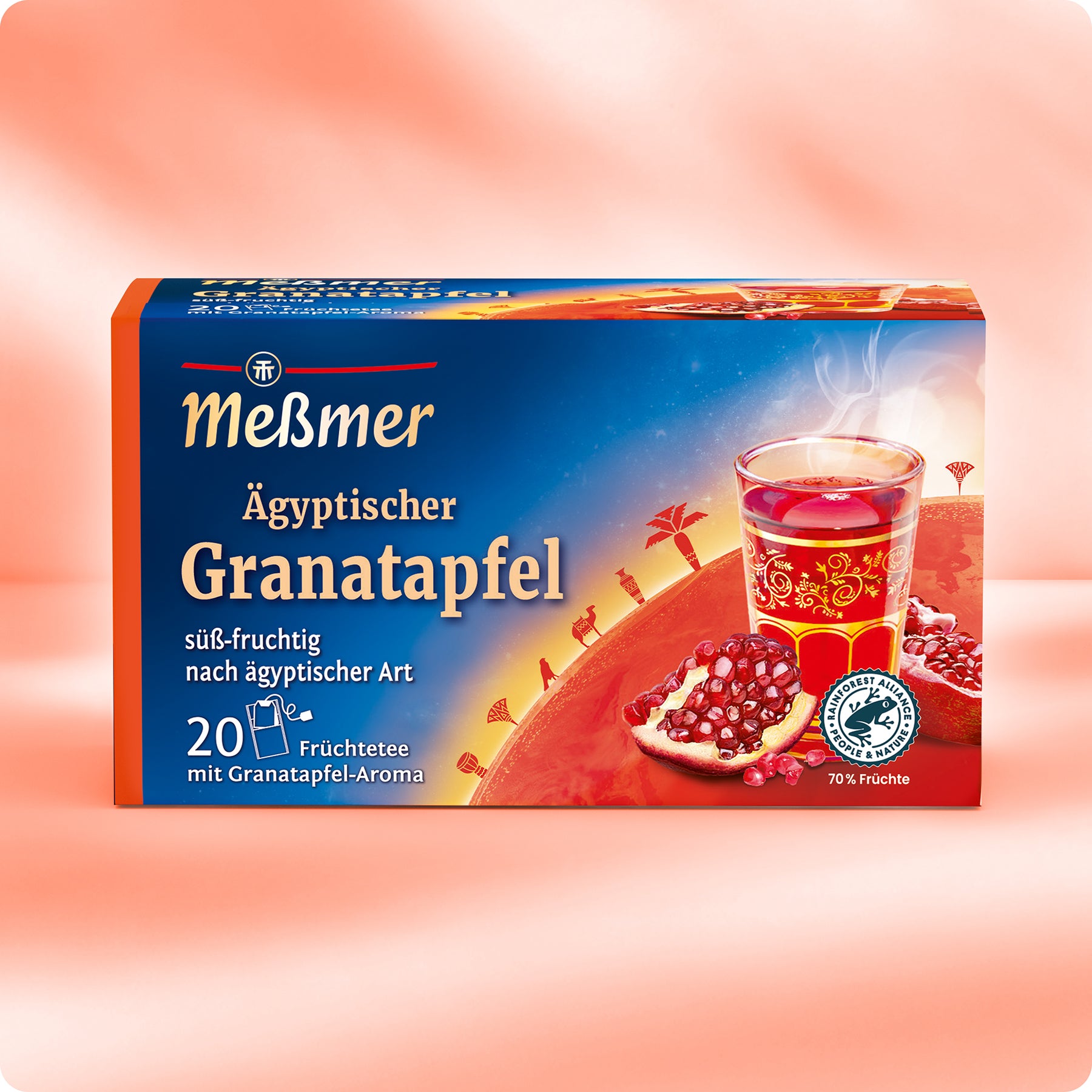 Eine Schachtel Meßmer DE Ägyptischer Granatapfel mit einem Glas roten Tees, einem aufgeschnittenen Granatapfel und ägyptisch inspirierter Kunst auf der Vorderseite vor einem orange-roten Hintergrund.