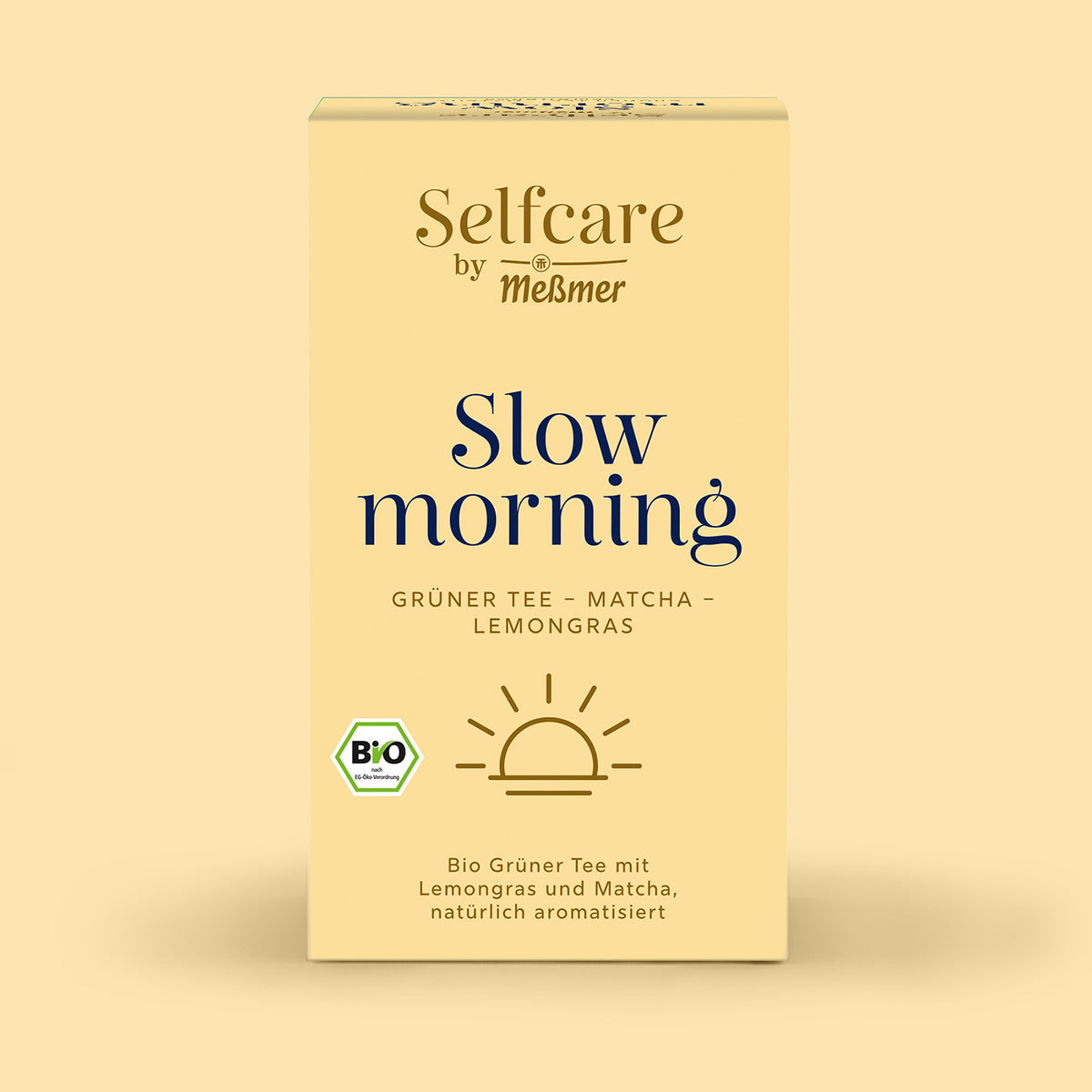 Verpackung von Bio Slow Morning mit Bio-Siegel, Sonnenmotiv und Hinweis auf grünen Tee mit Matcha und Lemongras, präsentiert auf hellem, warmem Hintergrund für einen entspannenden Start.